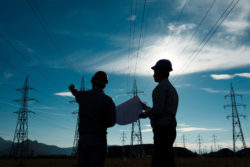 Two workers stand beneath power lines.