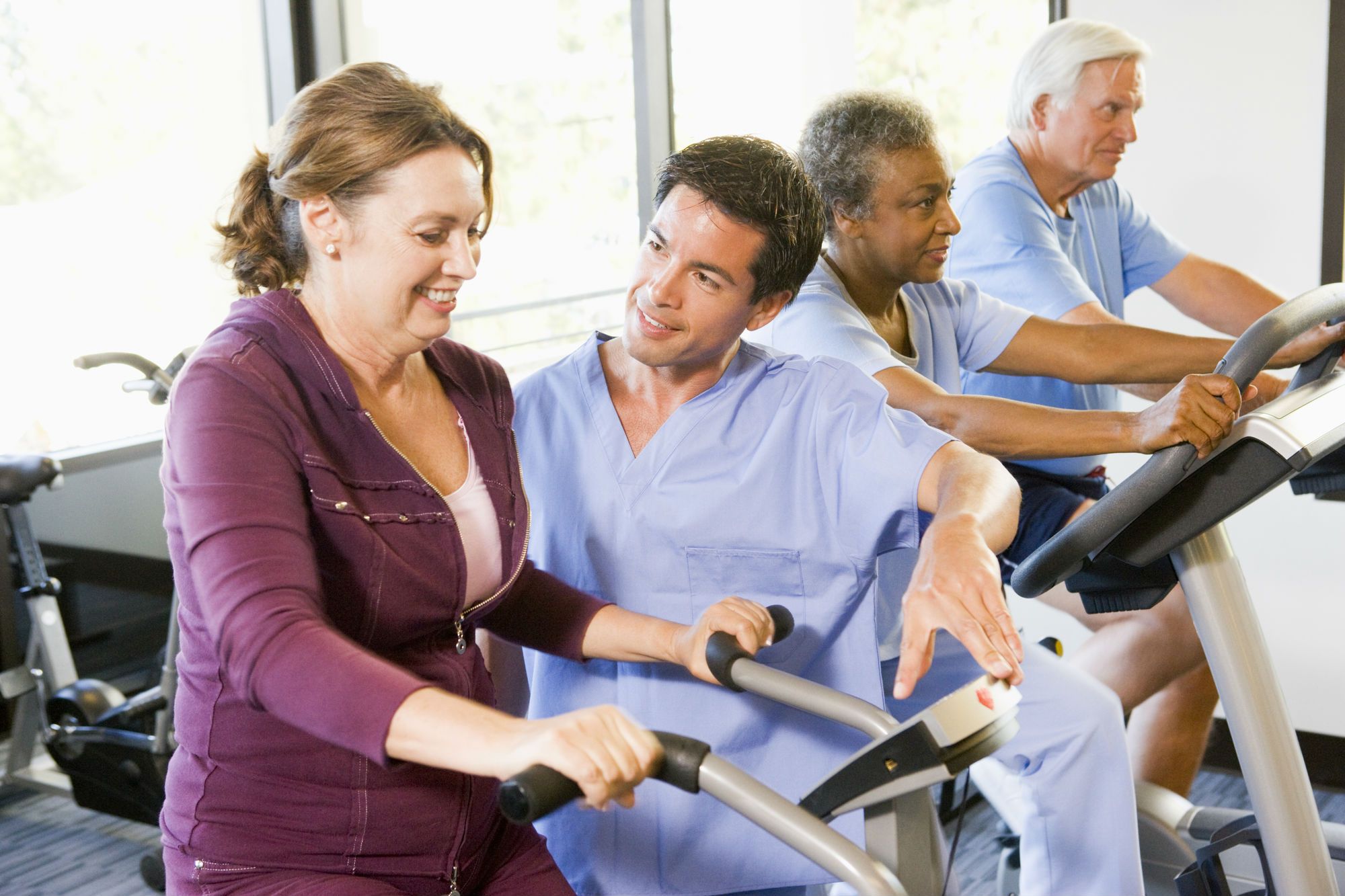 A physical therapist helps a woman on a stationary bike.