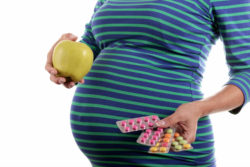 Pregnant woman holding vitamins and an apple