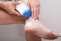 A woman puts talcum powder on her foot.