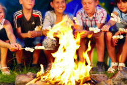 Boys sit around a campfire roasting marshmallows.
