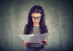 A woman looks shocked as she reads papers.