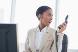 A woman makes a face at a phone receiver.