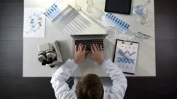 A lab worker types at a laptop.
