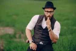 Bearded man vapes in middle of a grassy field.