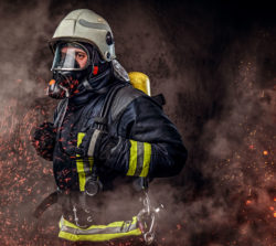 Firefighter in protective gear and oxygen mask makes his way among embers