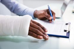 close up of broken arm man filling out disability insurance form on clipboard
