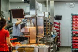 Two workers scramble to make food in a fast-food kitchen area.