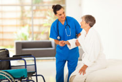 A doctor offers to help an elderly woman into a wheelchair.