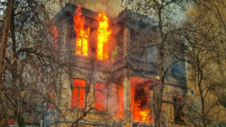 old-two-story-house-burns-surrounded-by-dead-trees