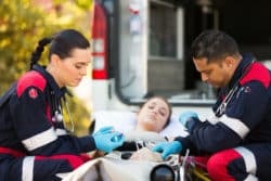 Female and male EMTs provide aid to a female patient on a stretcher.