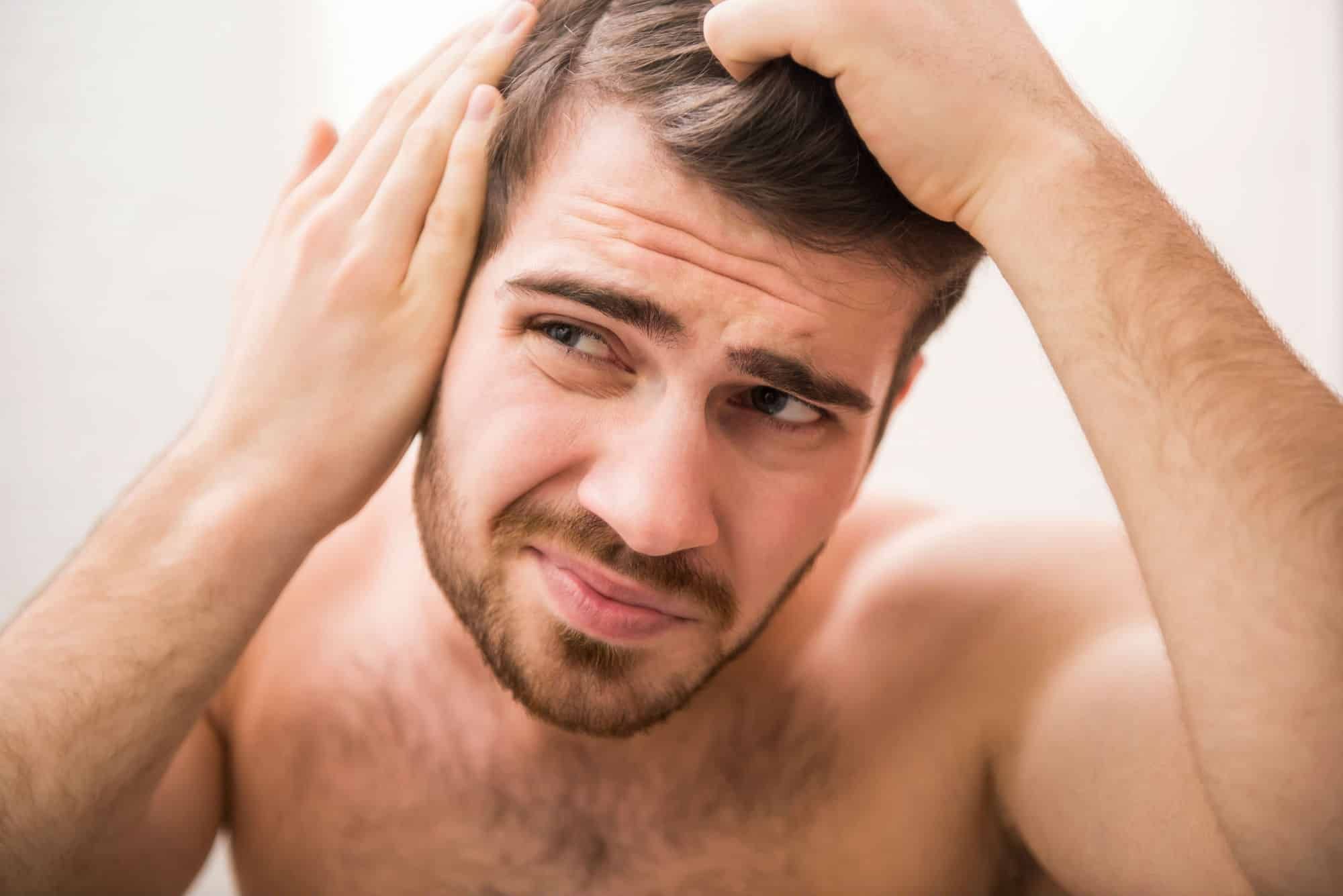 A man checks the skin at his hairline in the mirror.