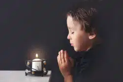 Small boy prays in front of lit candle.