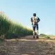 A teen boy wearing a backpack walks away and down a dirt path next to wildflowers