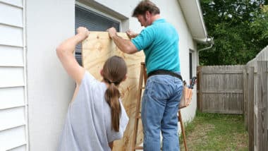 Two men apply plywood to a window in preparation for a hurricane