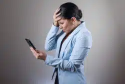 Businesswoman looks frustrated while looking at cell phone.