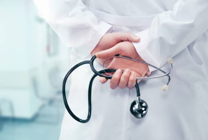 doctor holding stethoscope from behind regarding hospital strip-search settlement