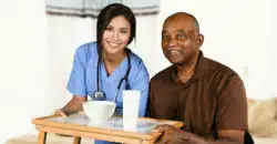 Female health care worker brings food tray to elderly male resident