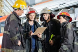 Firefighters in gear read a clipboard of instructions at the fire station