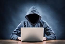 Hacker with blacked out face on laptop