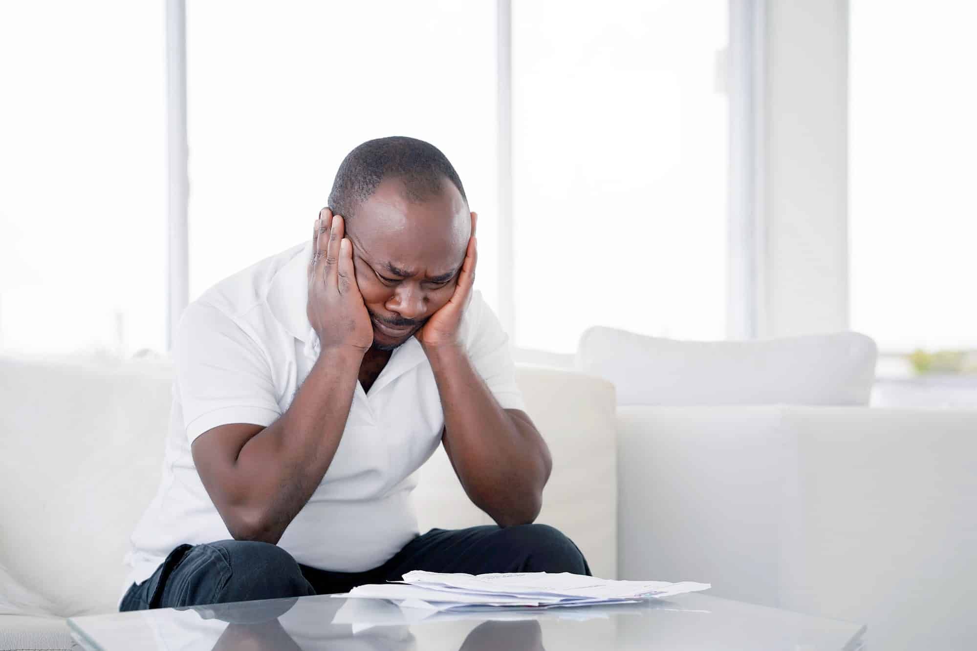 Man looks upset, holding his face in his hands as he leans over a pile of papers - long term disability