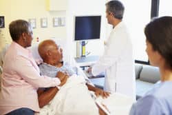 Senior male patient in hospital bed with wife at his side reviews computer screen with doctor