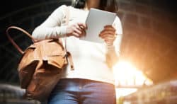 A woman holds a bag and a tablet.