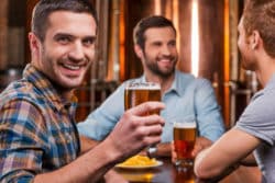 Young man toasting with a beer and two friends with beer in background.