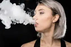A young woman breathes out a cloud of vapor.