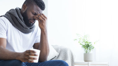 Feverish man holds his head and drinks cup of tea