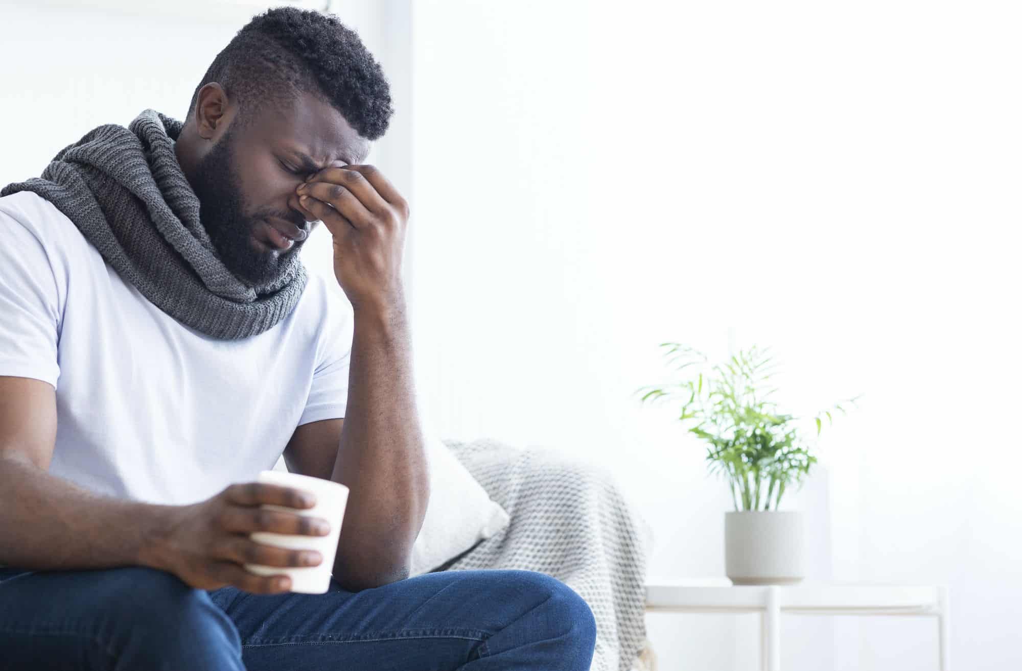 Feverish man holds his head and drinks cup of tea