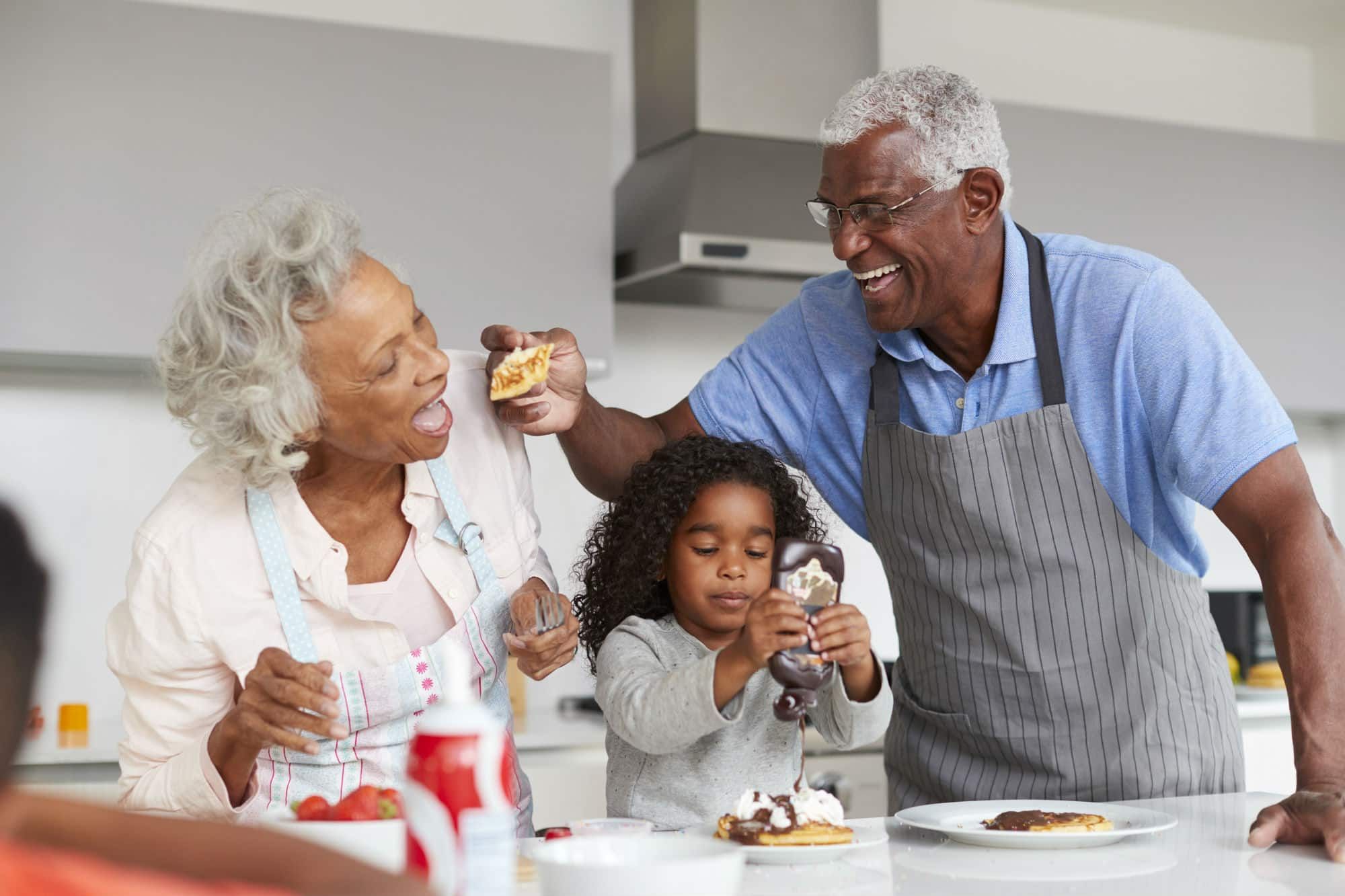 Grandpa shares pancake with grandma while granddaughter pours chocolate syrup on her pancake