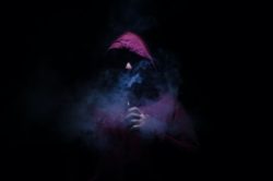 Man in purple hoodie with black background blows vape cloud