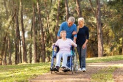 Mature couple takes mom in wheelchair for walk in the woods
