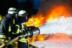 Two firefighters apply foam.