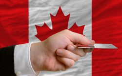 Hand holding credit card in front of Canadian flag regarding the economic aid package passed for workers impacted by the COVID-19 pandemic