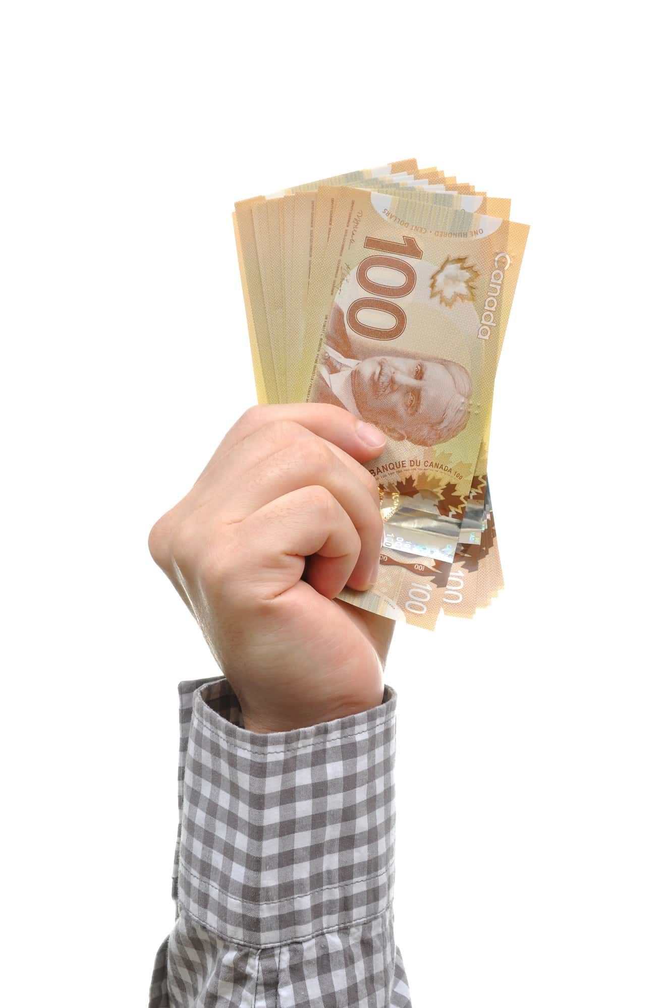 Hand holding money regarding the massive $107 billion aid package passed to help Canadians as they cope with job losses and other economic challenges during the COVID-19 pandemic