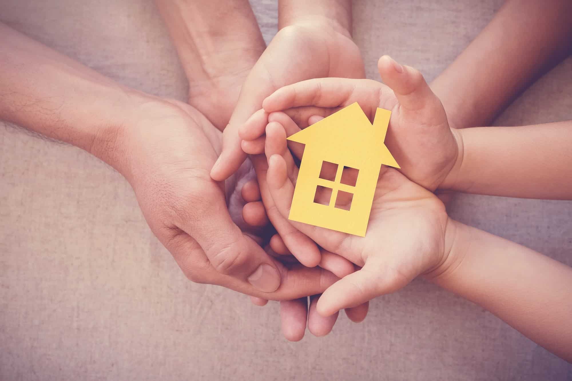 multiple hands holding a small house regarding the group of habitat for humanity residents allowed to stay in their homes amid the pandemic and a pending class action lawsuit