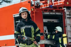 Male firefighter holds hose as colleague checks equipment on the fire truck