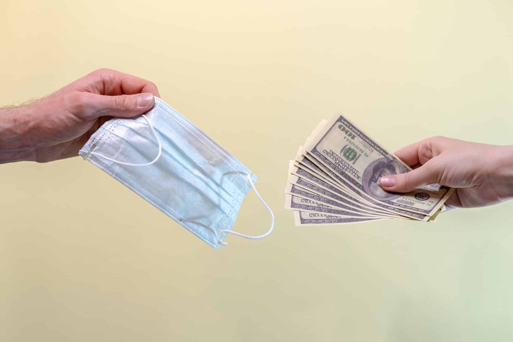 Person exchanging cash for face mask regarding Canada's competition bureau cracking down on price gouging 