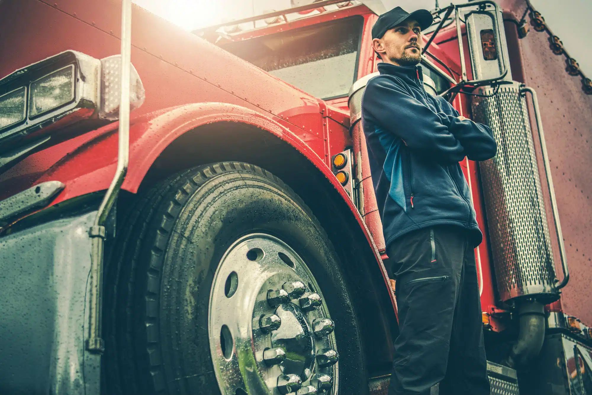 A truck driver stands in front of a truck.
