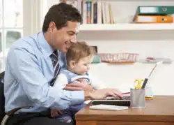 Dad working from home on laptop holding kid
