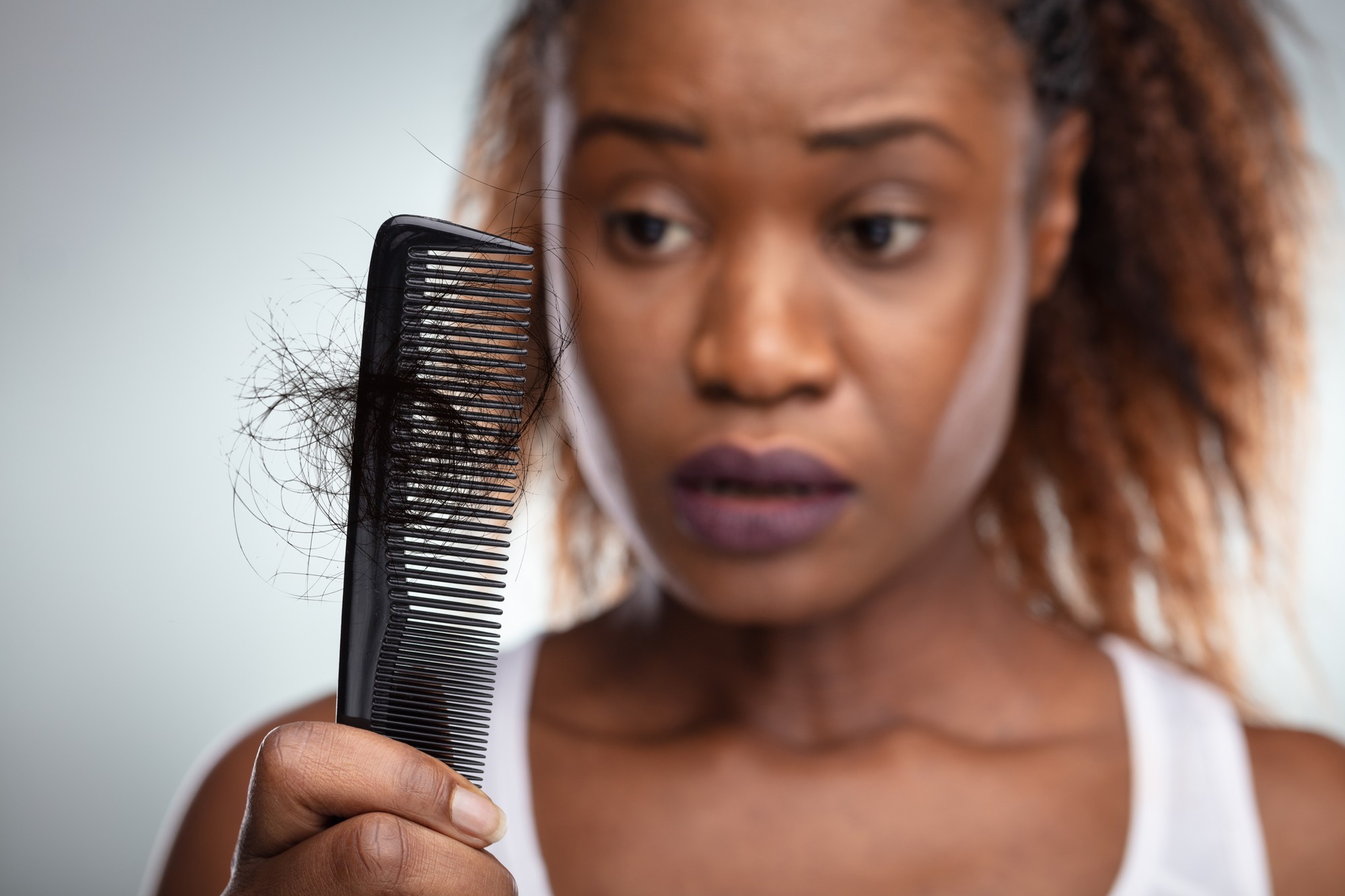 Woman looking at hair loss in comb regarding Deva Concepts class action lawsuit accusing the companies DevaCurl products of causing hair loss and damage