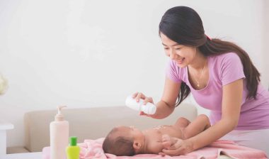 Mother sprinkles powder on baby's tummy