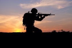 Silhouette of soldier pointing gun at sunset