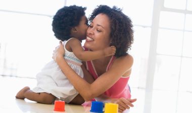 Mom hugs baby daughter playing with colorful blocks