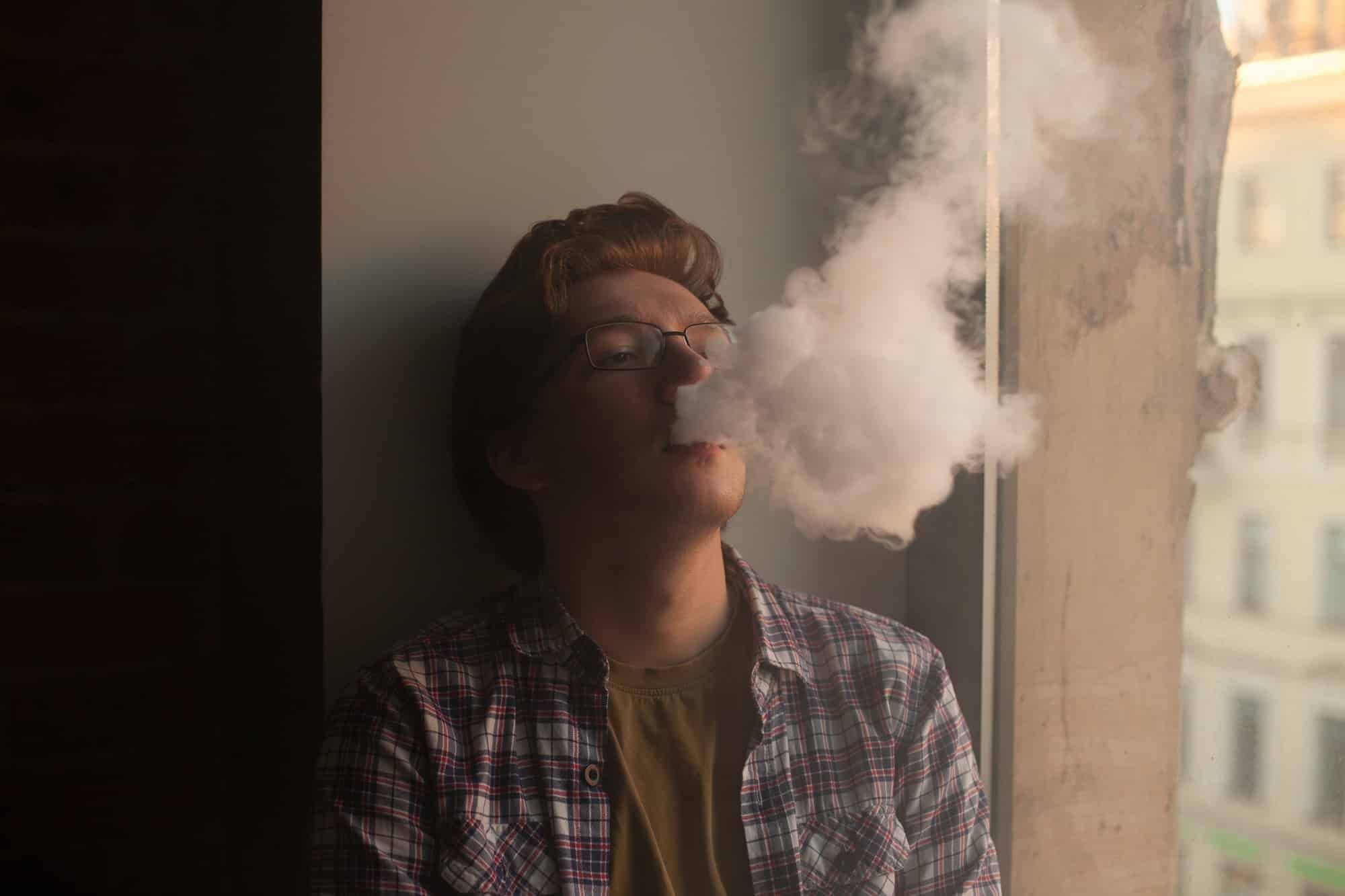 Young man leans against a wall and vapes