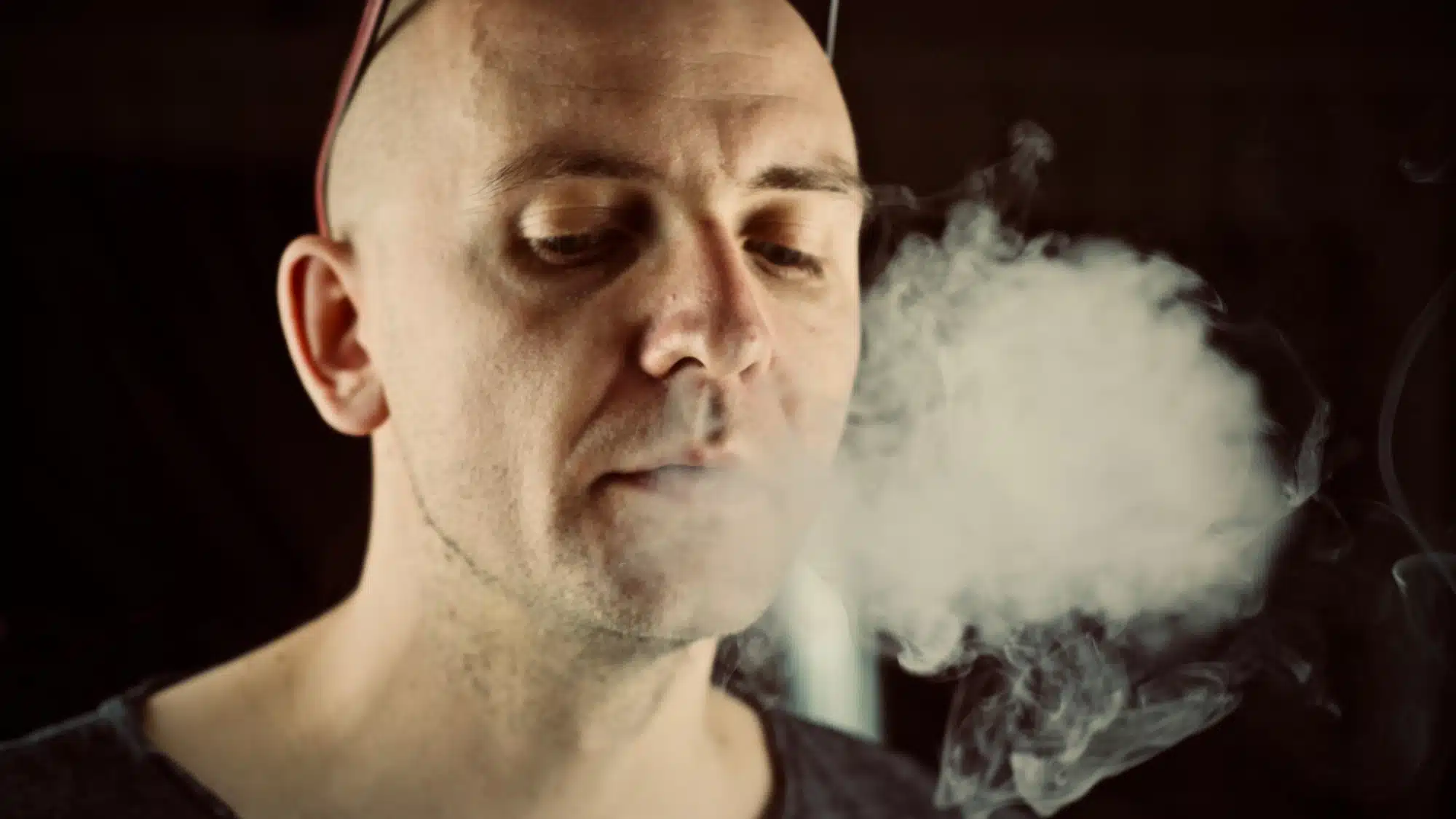 Older bald man exhales vaping cloud