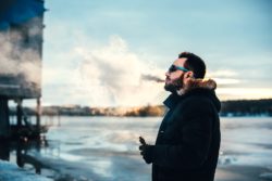 Bearded young man puffs one cigarette near a river