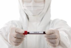 Gloved hands hold vial of blood labeled COVID19